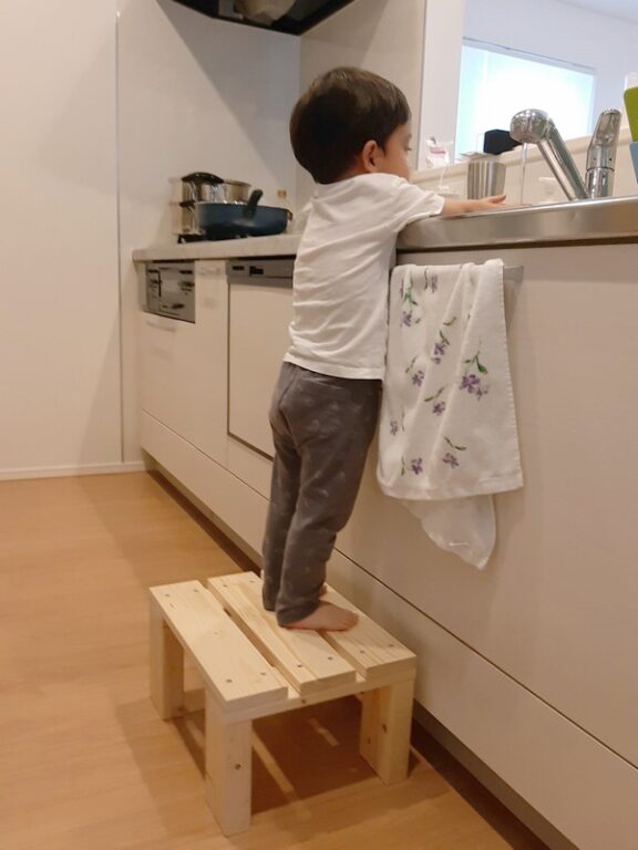 キッチンで、幼児が踏み台に上がって手洗いするところ。